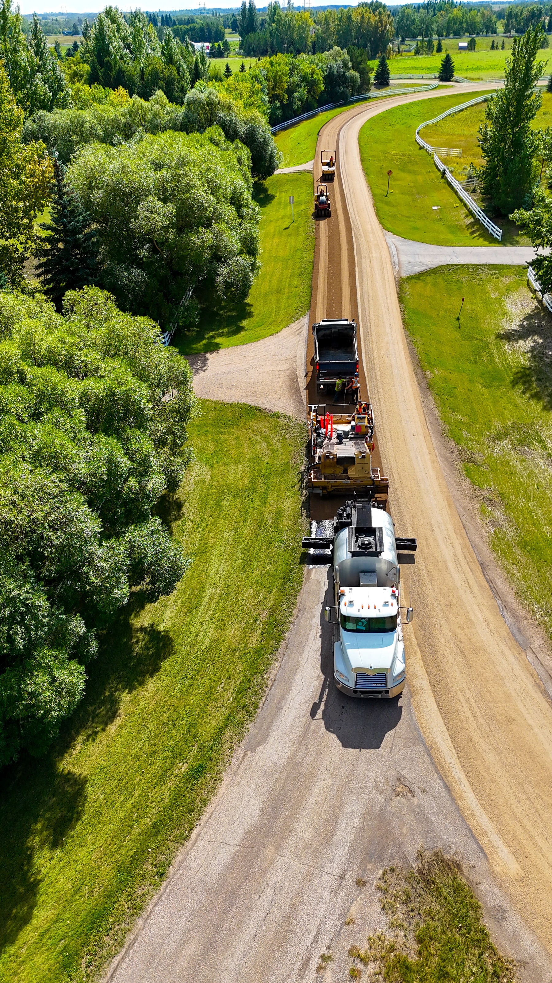 Chip seal crew laying a new wearing surface on a tree-lined country road, seen from above