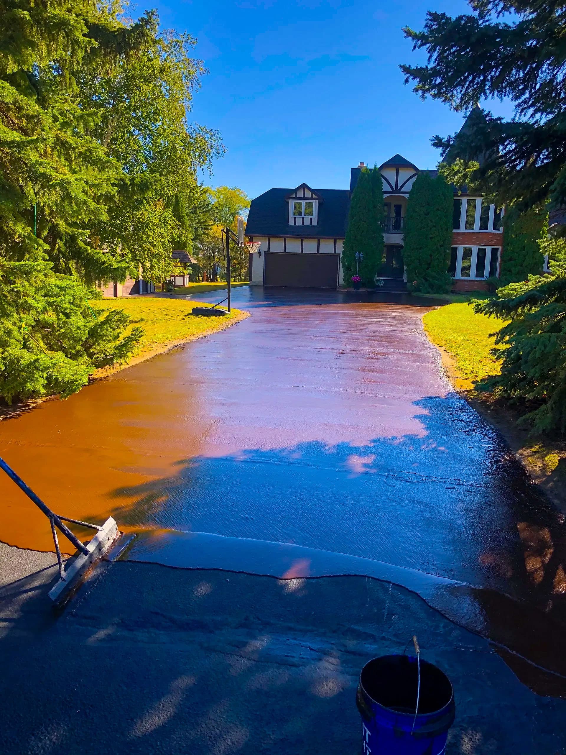 Freshly seal-coated residential driveway with a deep black finish in front of a two-storey home