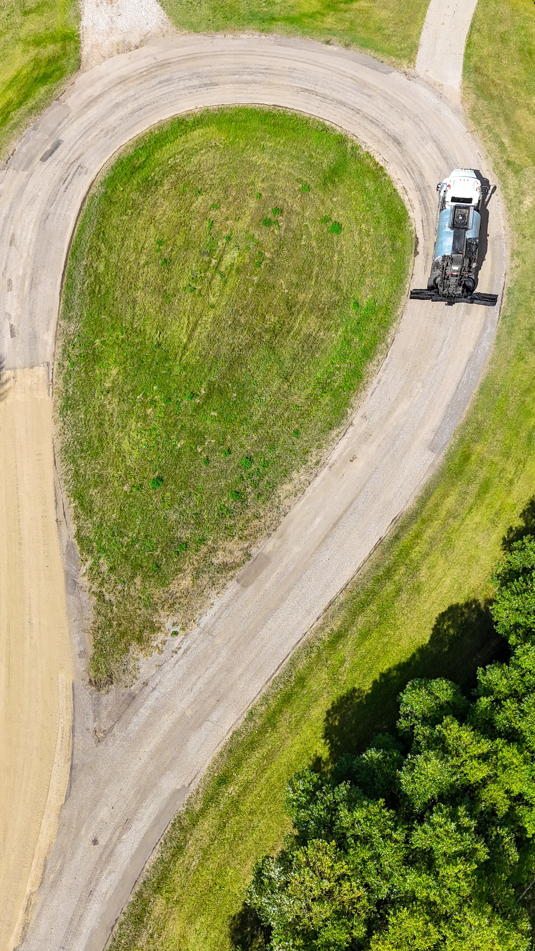 Spray truck treating a curving gravel loop on an acreage, seen from above